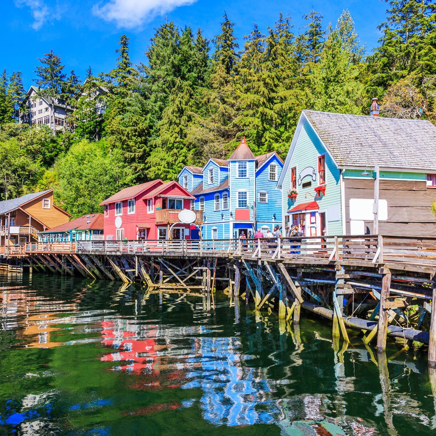 Colorful wooden houses on stilts reflecting in calm water under a sunny sky.